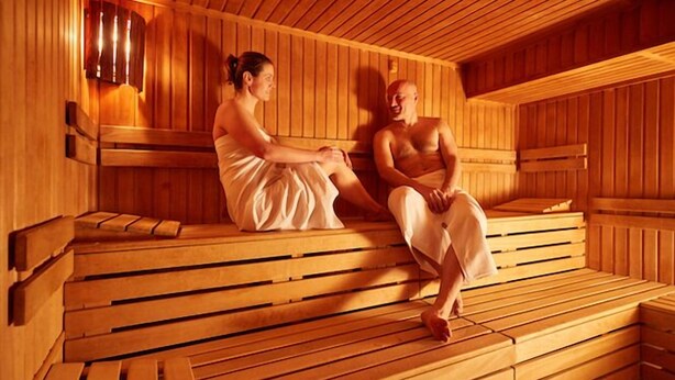 Una sauna con bancos de madera y asientos, un asiento con una toalla y un asiento con una toalla.