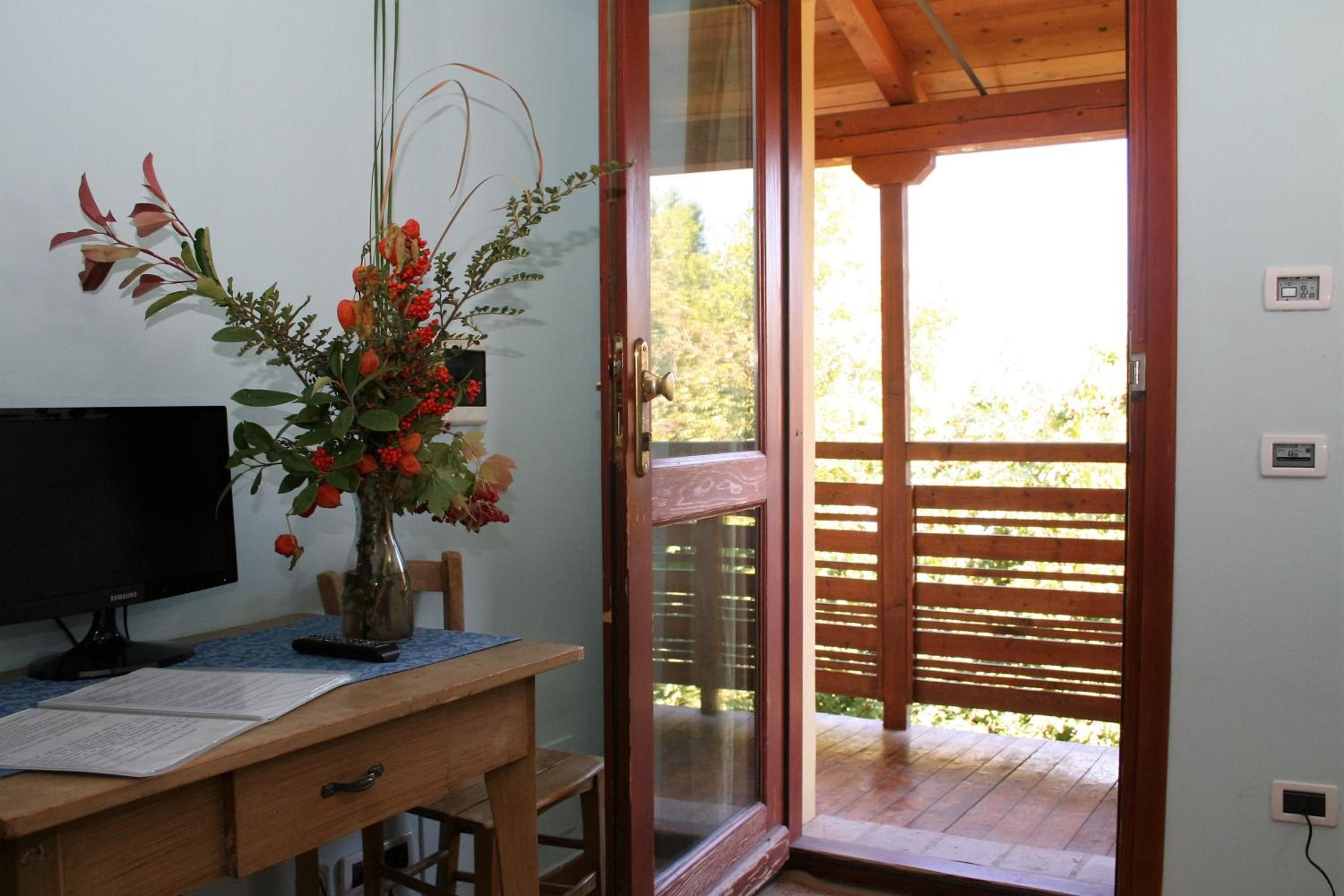 A room with a wooden desk, a computer monitor, a vase with flowers, and a sliding glass door leading to an outdoor area.