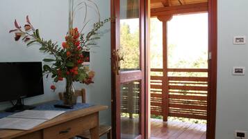 A room with a wooden desk, a computer monitor, a vase with flowers, and a sliding glass door leading to an outdoor area.