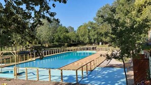 A rectangular swimming pool with a wooden deck and safety railings, surrounded by trees.
