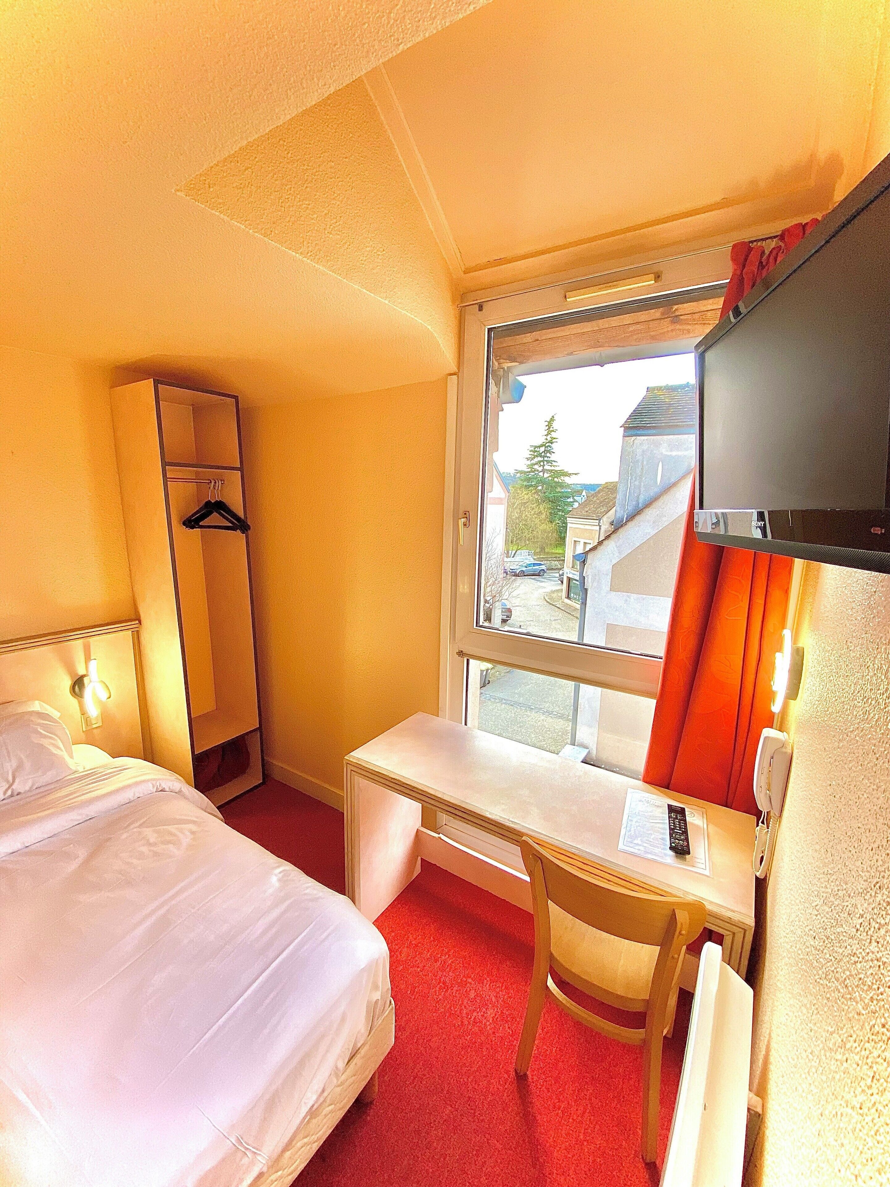 Una habitación de hotel con cama, escritorio, silla, televisor y armario.