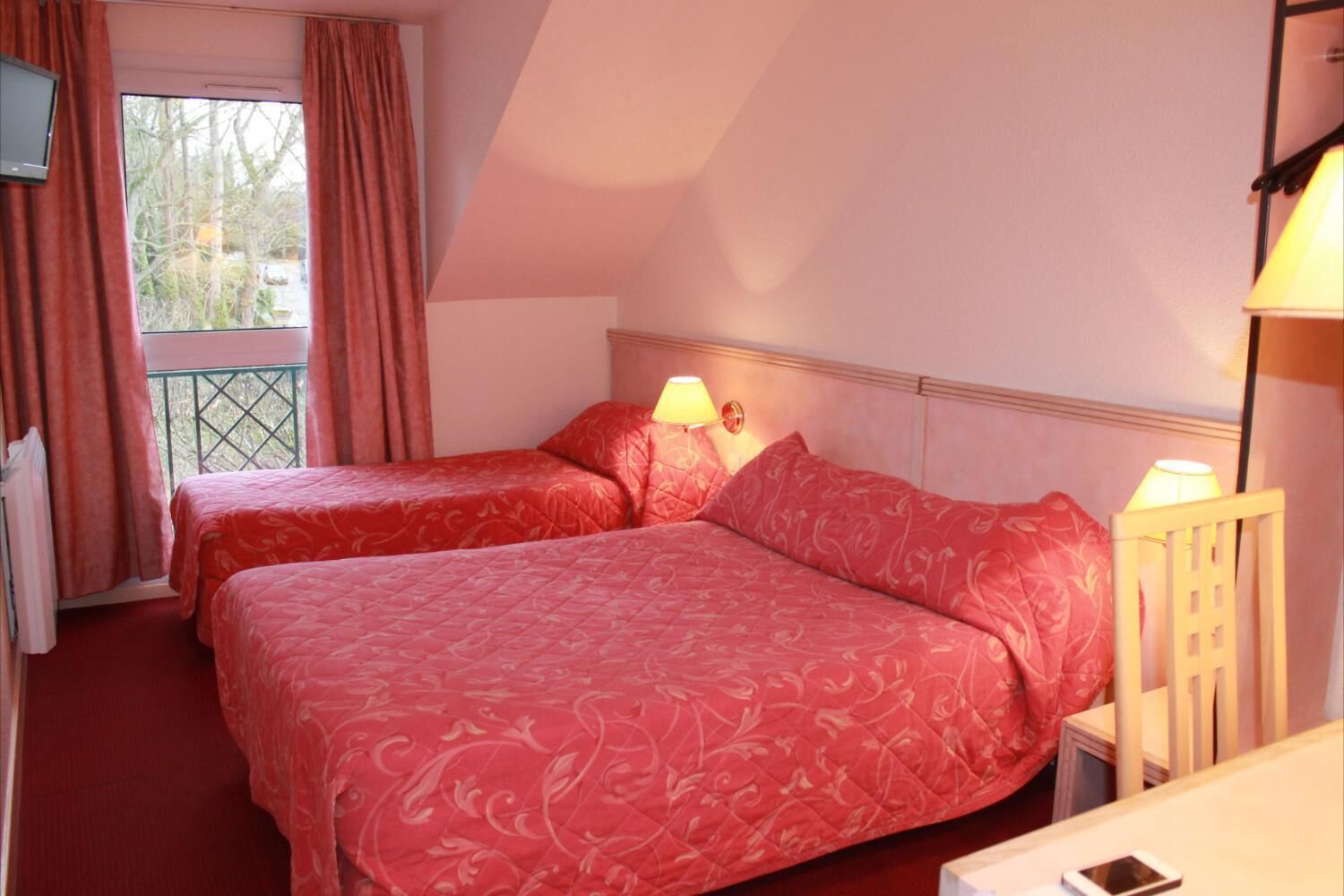 Een hotelkamer met twee bedden, een balkon en uitzicht op bomen.