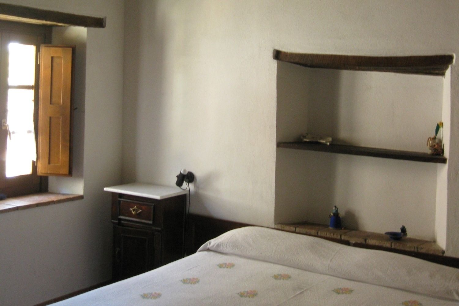 A bedroom with a bed, a wooden cabinet, a shelf, and a window.