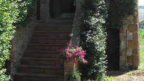 A stone building with a staircase leading to a door, surrounded by greenery and flowers. - Agriturismo Le Spighe (Proceno)