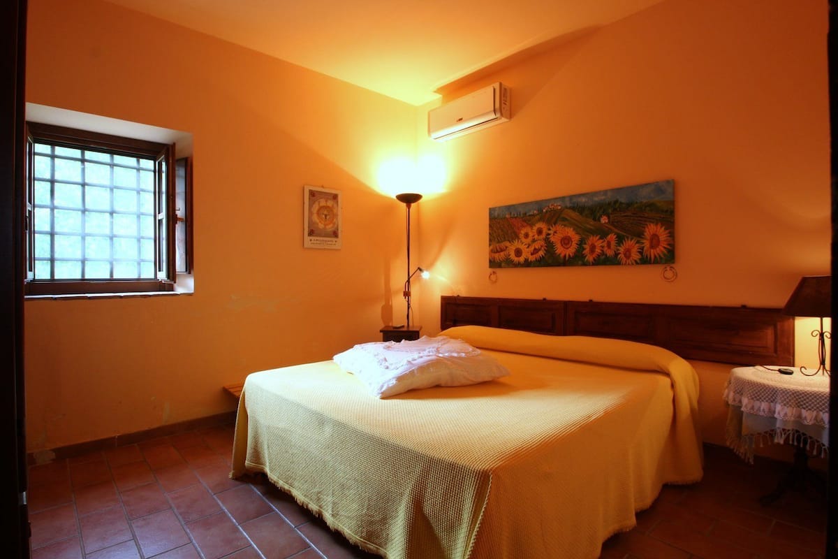 A bedroom with a bed, a nightstand, a lamp, a painting, and a window.