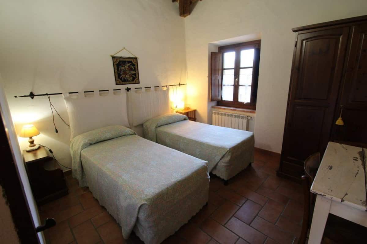 A bedroom with two single beds, a radiator, a window, and a wooden wardrobe.