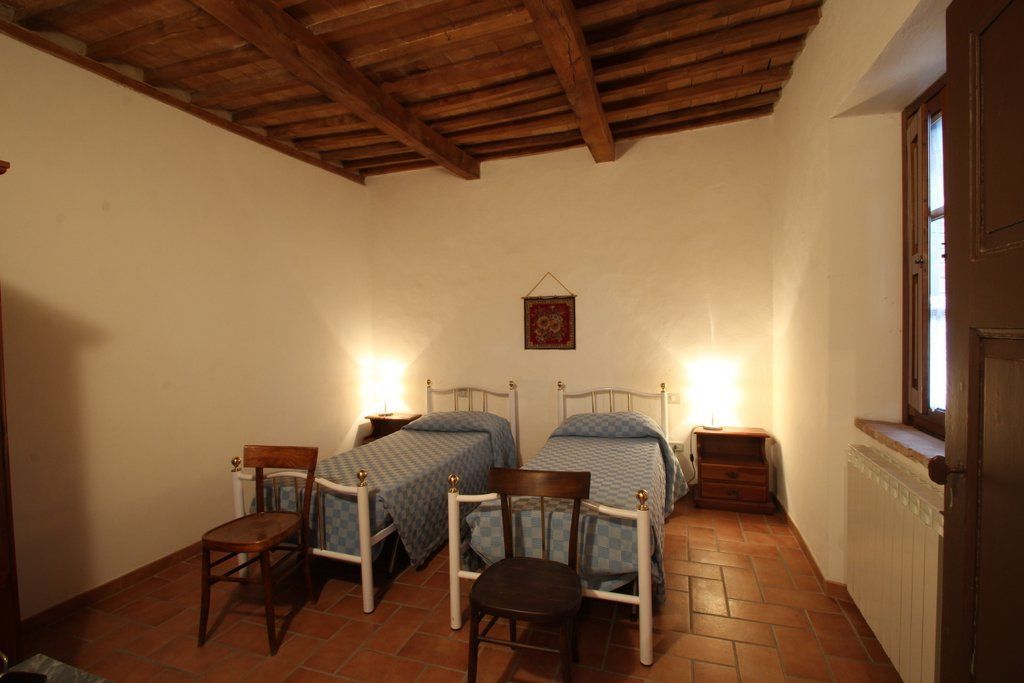 A bedroom with two beds, wooden chairs, a small table, and a radiator.