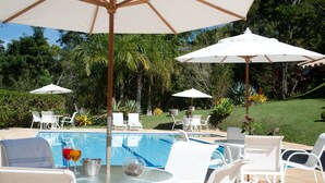 A poolside area with white chairs and umbrellas, surrounded by lush greenery. - Pousada Les Roches (Petrópolis)