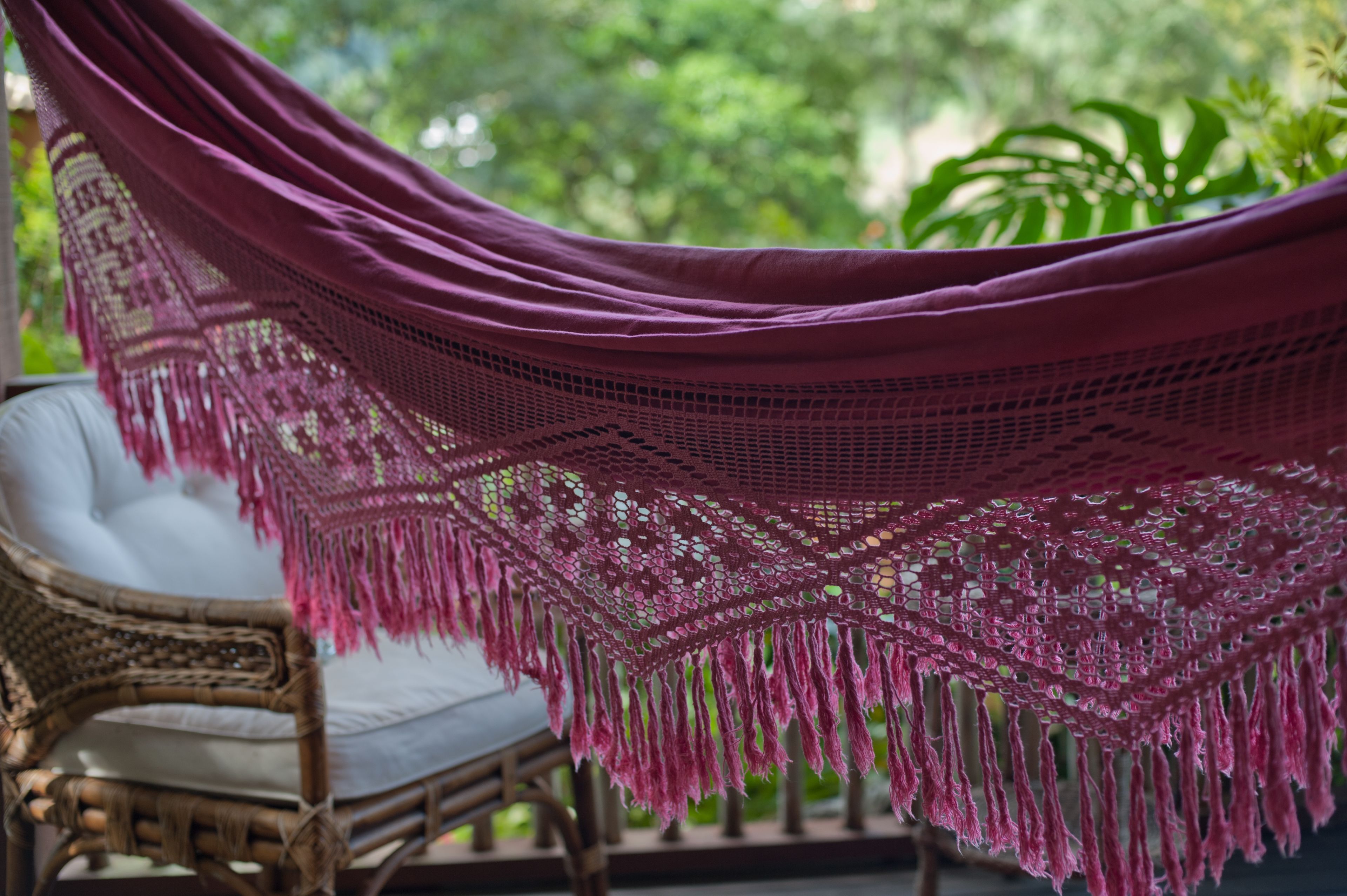 A wicker chair with a white cushion and a purple hammock with fringe.