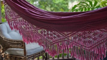 A wicker chair with a white cushion and a purple hammock with fringe.