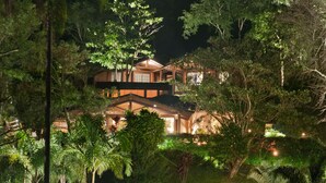 A multi-story building surrounded by dense foliage at night. - Pousada Les Roches (Petrópolis)