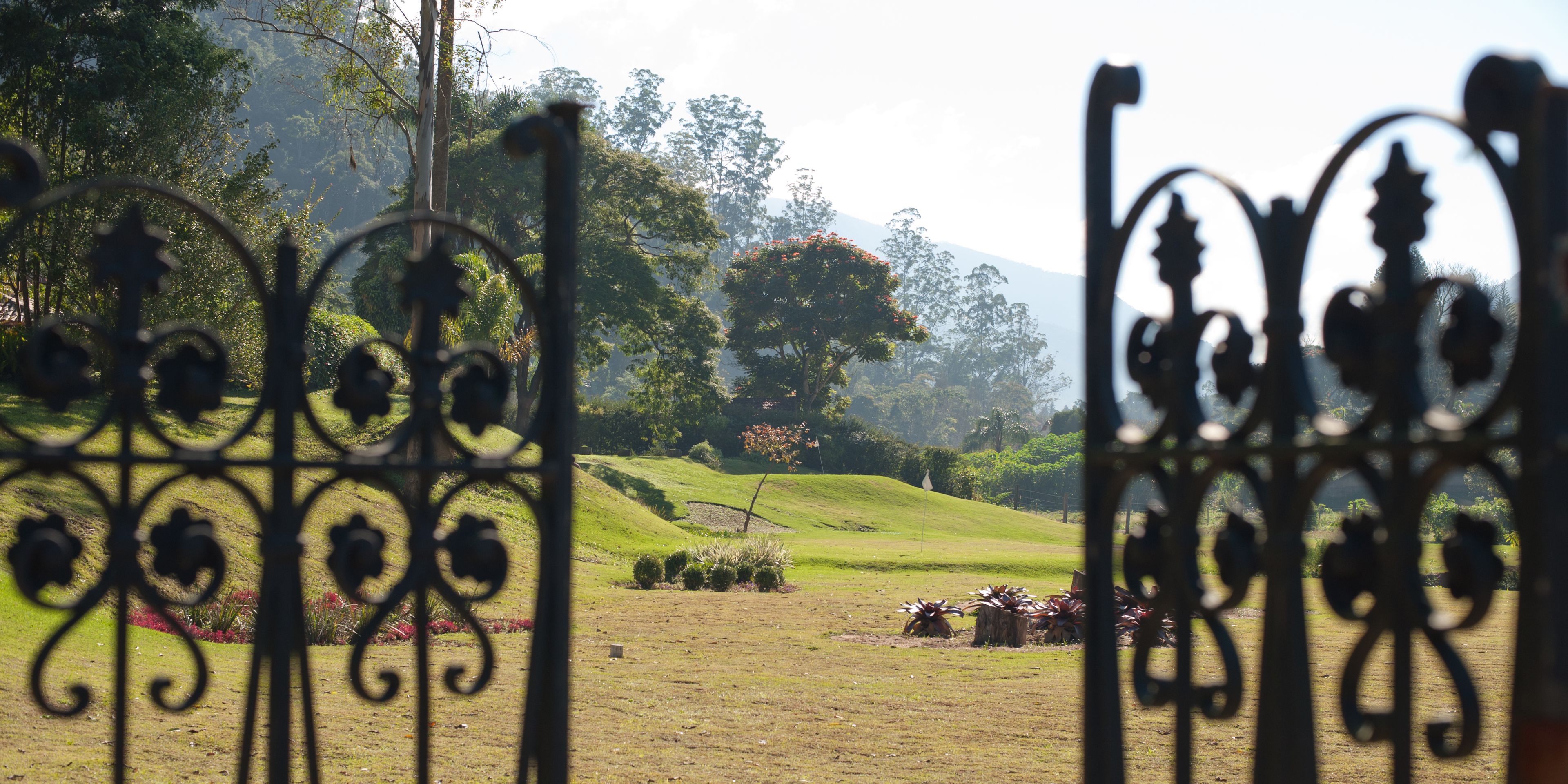 A view through ornate metal gates into a lush, green landscape with rolling hills and trees.