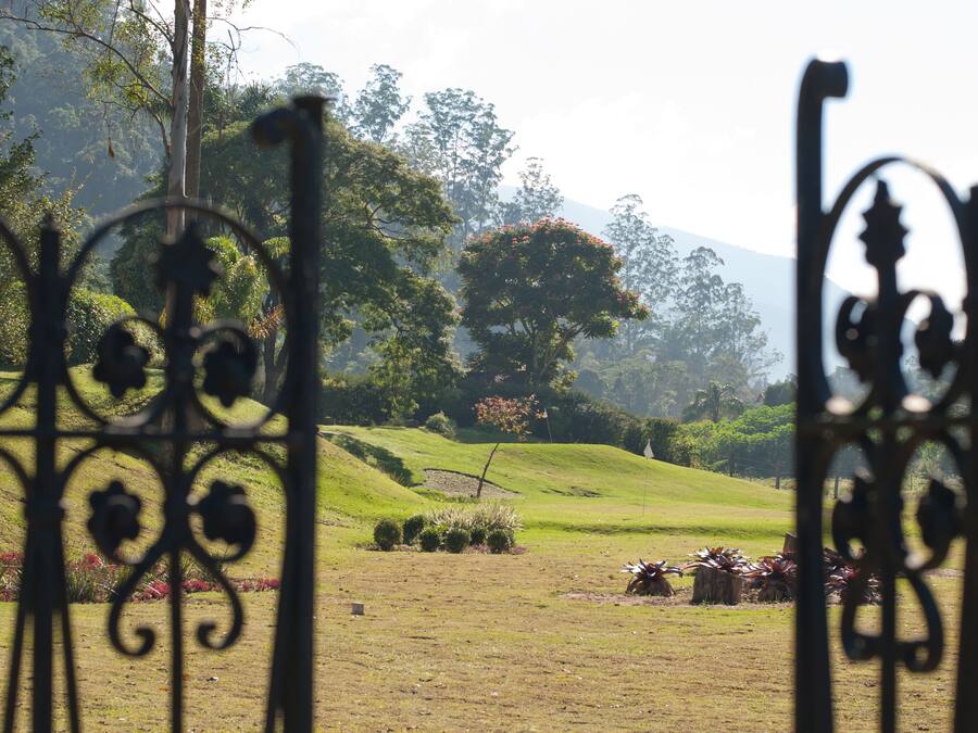 A view through ornate metal gates into a lush, green landscape with rolling hills and trees.