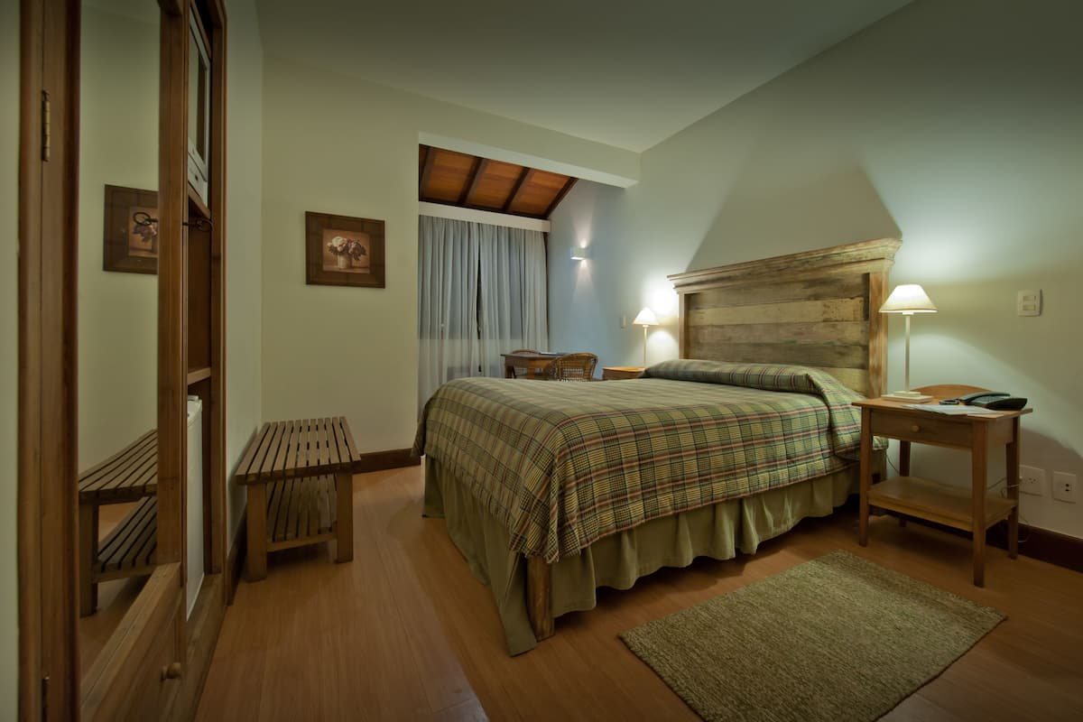 Ein Schlafzimmer mit Bett, Nachttisch, Lampe, Bank und einem hölzernen Kopfteil.