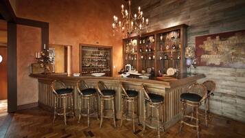 Una zona de bar con taburetes de madera, una botellera y una araña.