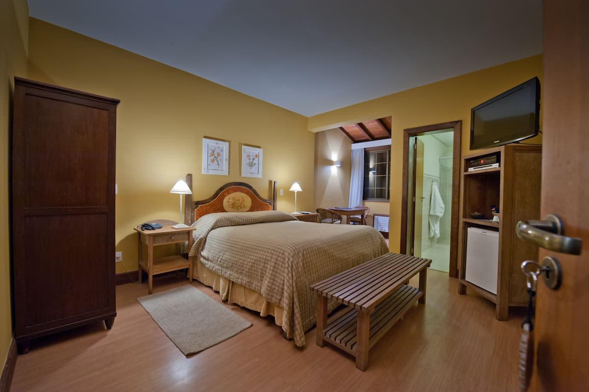 Ein Schlafzimmer mit einem Bett, Nachttischen, einer hölzernen Bank, einem Schreibtisch, einem Fernseher und einem Kleiderschrank.