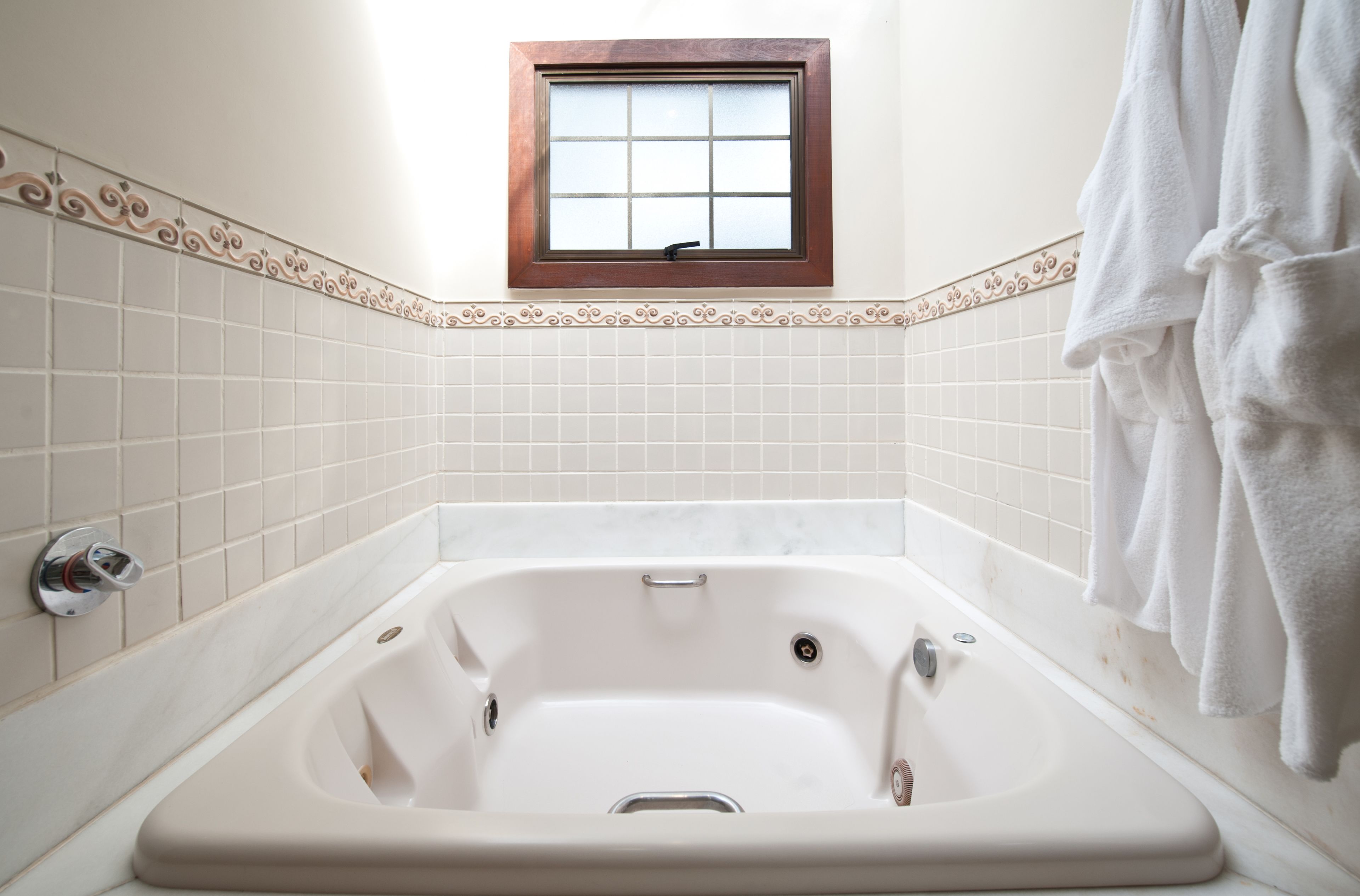 A bathroom with a white bathtub, a small window, and a towel hanging on the wall.