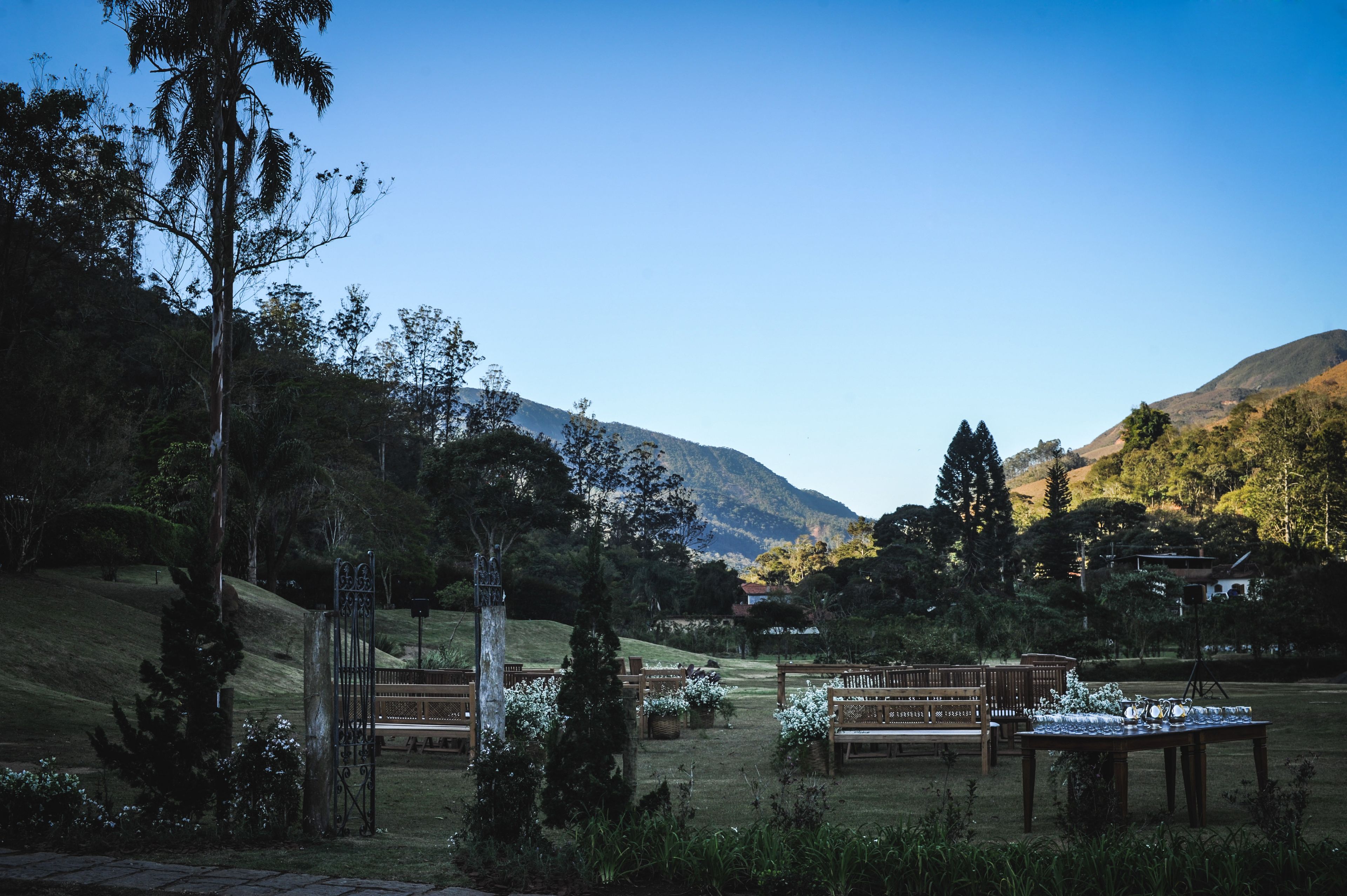 Un espacio al aire libre con bancos y mesas de madera, rodeado de follaje y un paisaje montañoso.