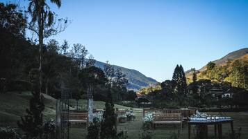 Un espacio al aire libre con bancos y mesas de madera, rodeado de follaje y un paisaje montañoso.