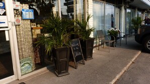 A storefront with a sign reading "OFFICE" and a "BUSINESS HOURS" sign listing operating times. There are potted plants outside and a "WELCOME to the [name]" sign on the sidewalk. - Catalina Motel (Sault Ste. Marie)