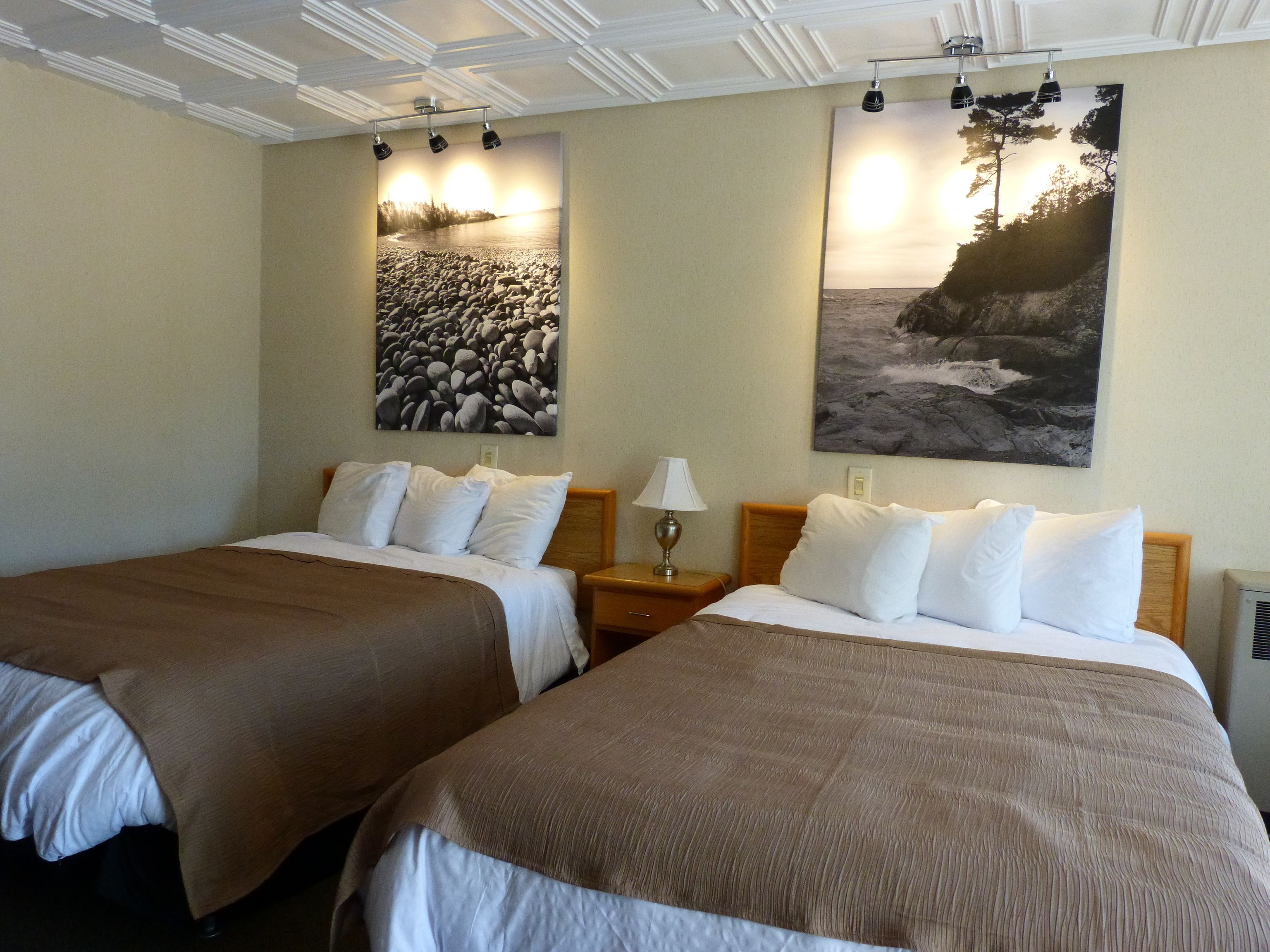 A hotel room with two beds, beige walls, and two large landscape paintings.