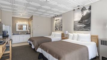 Une chambre d’hôtel avec deux lits, une kitchenette, une salle de bain avec un miroir et des luminaires, et des œuvres d’art accrochées aux murs.