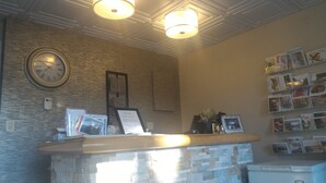 A reception area with a stone counter, a clock, framed pictures, and a wall of postcards. - Catalina Motel (Sault Ste. Marie)