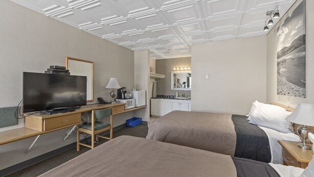 A hotel room with two beds, a desk with a television, a kitchenette, and a bathroom with a mirror and lights. - Catalina Motel (Sault Ste. Marie)