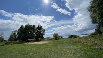 En gräsklädd åker med ett volleybollnät, träd och en klar himmel.