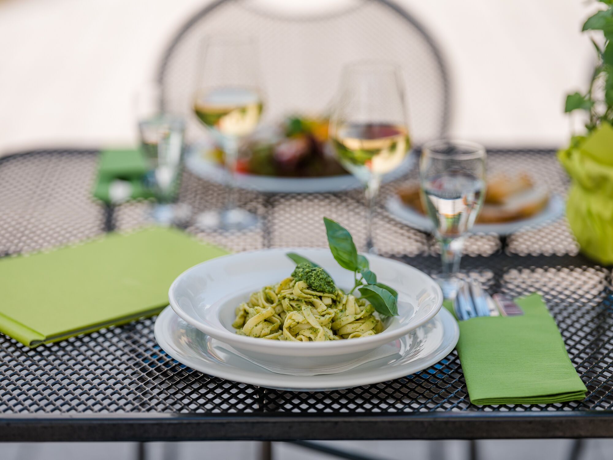 Una mesa de comedor con un plato de pasta, copas de vino y una servilleta verde.