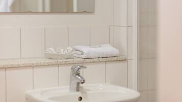 Une salle de bain avec un lavabo blanc, un miroir au-dessus et un porte-serviettes avec des serviettes pliées.
