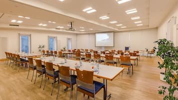 A conference room with multiple tables and chairs, a projector screen, and a large window.