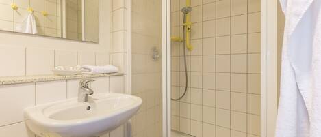 Un baño con un lavamanos blanco, un espejo y una zona de ducha.