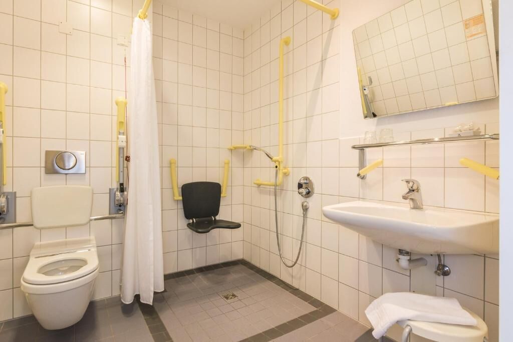 A small, tiled bathroom with a toilet, a sink, a shower, and a mirror.