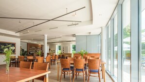 A spacious dining area with wooden tables and chairs, large windows offering views of the outdoors, and a bar area in the background. - Ferienpark Plauer See (Alt Schwerin)