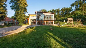 A modern building with a glass facade, a balcony, and a playground with a slide and swings. - Ferienpark Plauer See (Alt Schwerin)