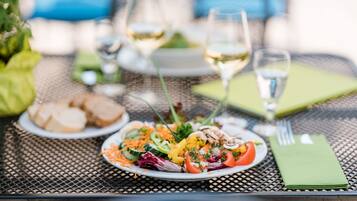 A dining table with a plate of salad, two glasses of white wine, and a folded green napkin.