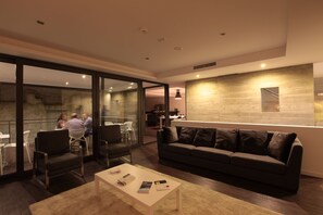 A modern living room with a sofa, coffee table, and chairs. There is a glass wall separating the living area from a dining area. - Casa Dona Maria Luiza (Torre de Moncorvo)