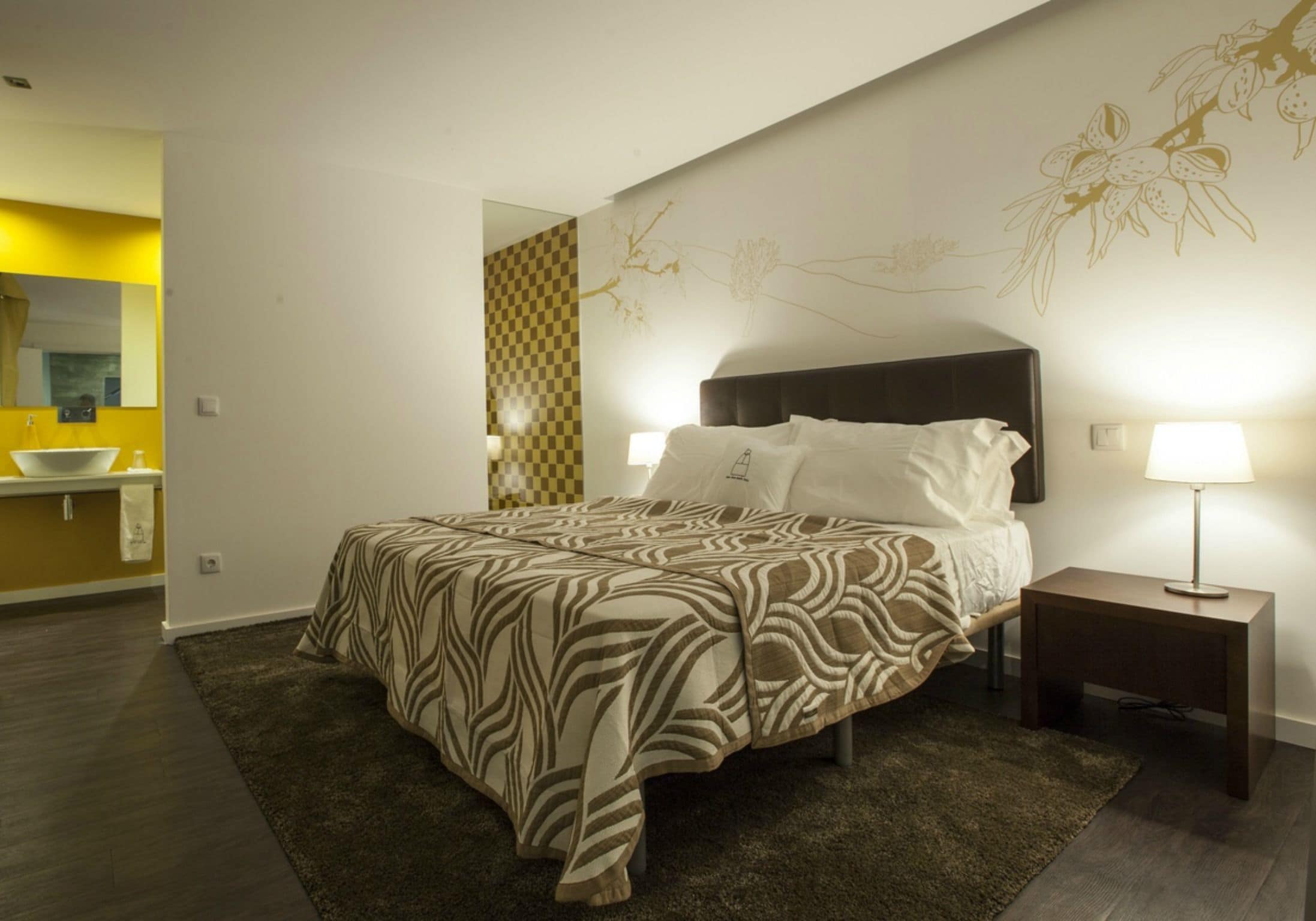A modern bedroom with a large bed, a bedside table with a lamp, and a bathroom visible through an open door.