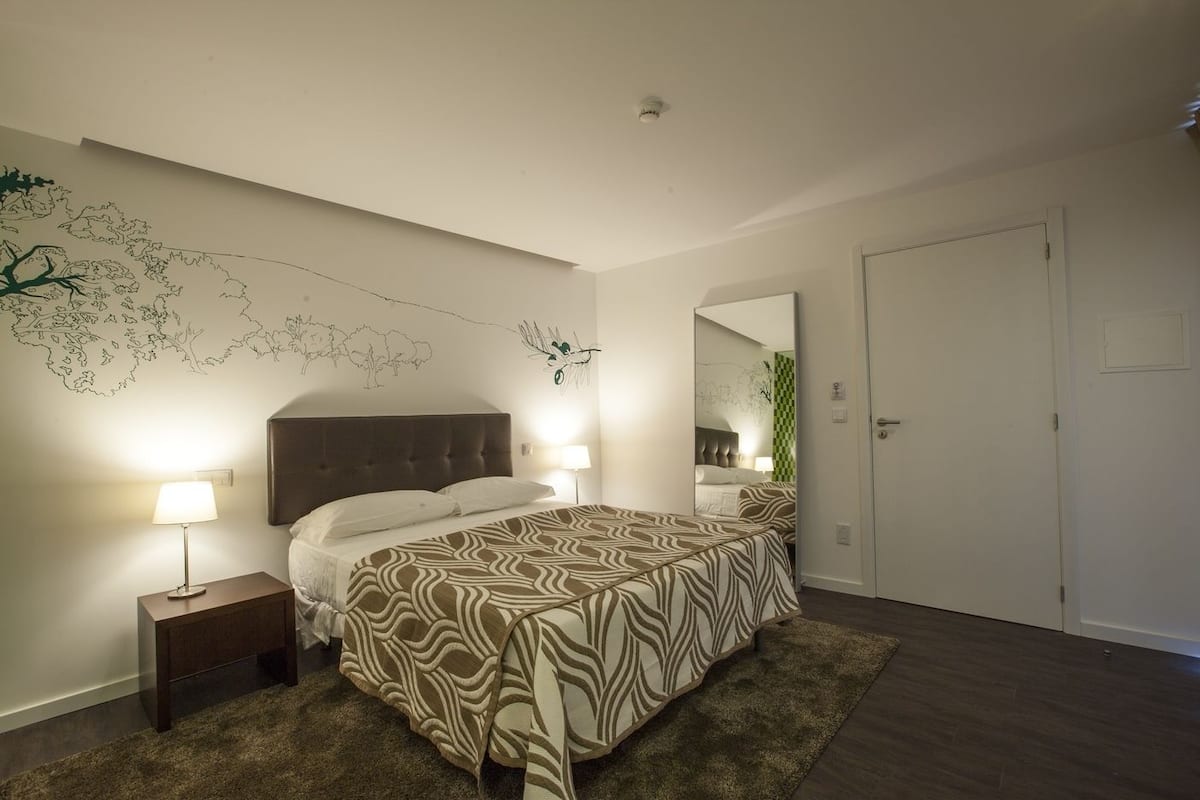 Ein Schlafzimmer mit Bett, Nachttischen, Wandgemälde und einer Tür.