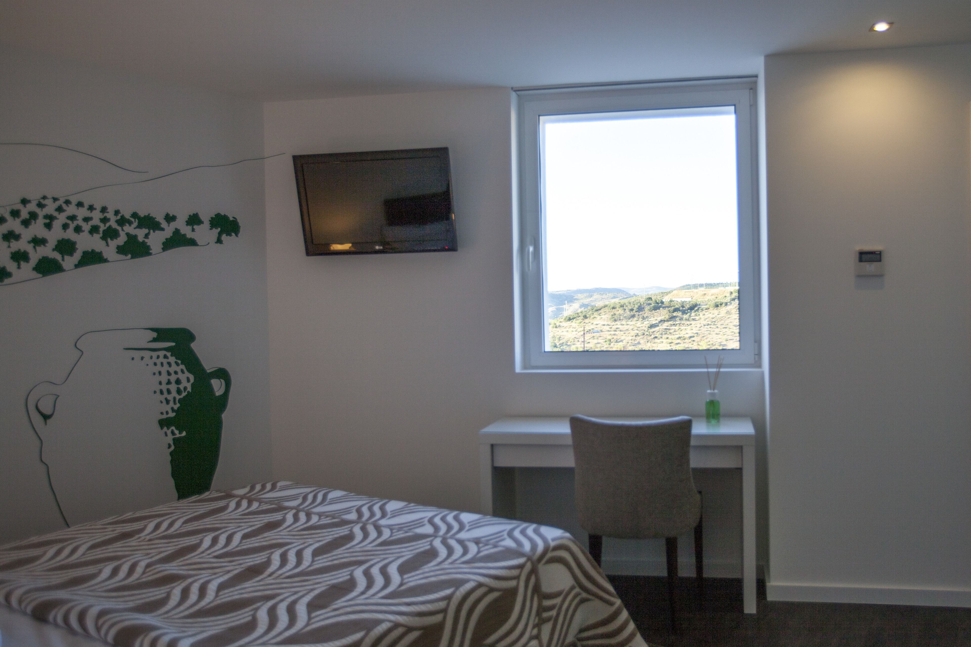 Een hotelkamer met een bed, een bureau, een stoel, een televisie en een raam met uitzicht op het platteland.