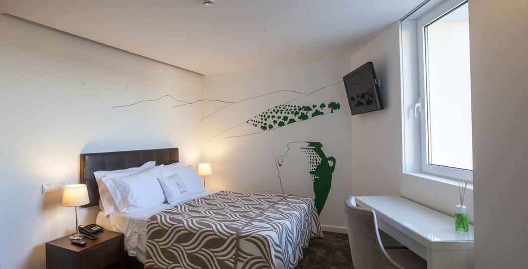 Una habitación de hotel con cama, mesita de noche, lámpara y ventana con vistas.