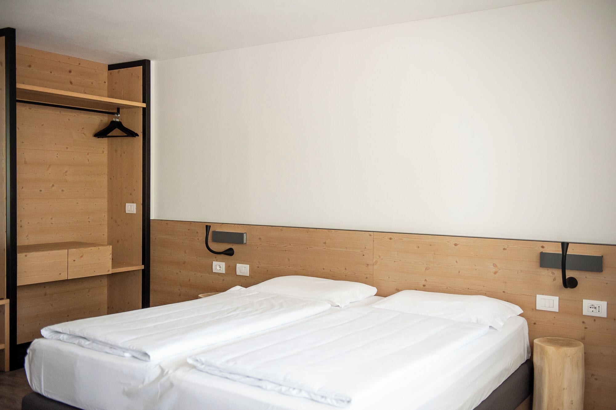 Une chambre à coucher au style minimaliste, avec deux lits, un lambris en bois et une armoire en bois.