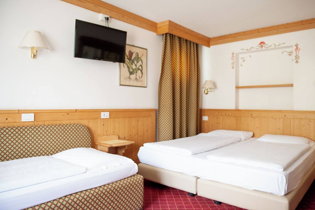 A hotel room with two single beds, a TV, a small table, and a patterned sofa.