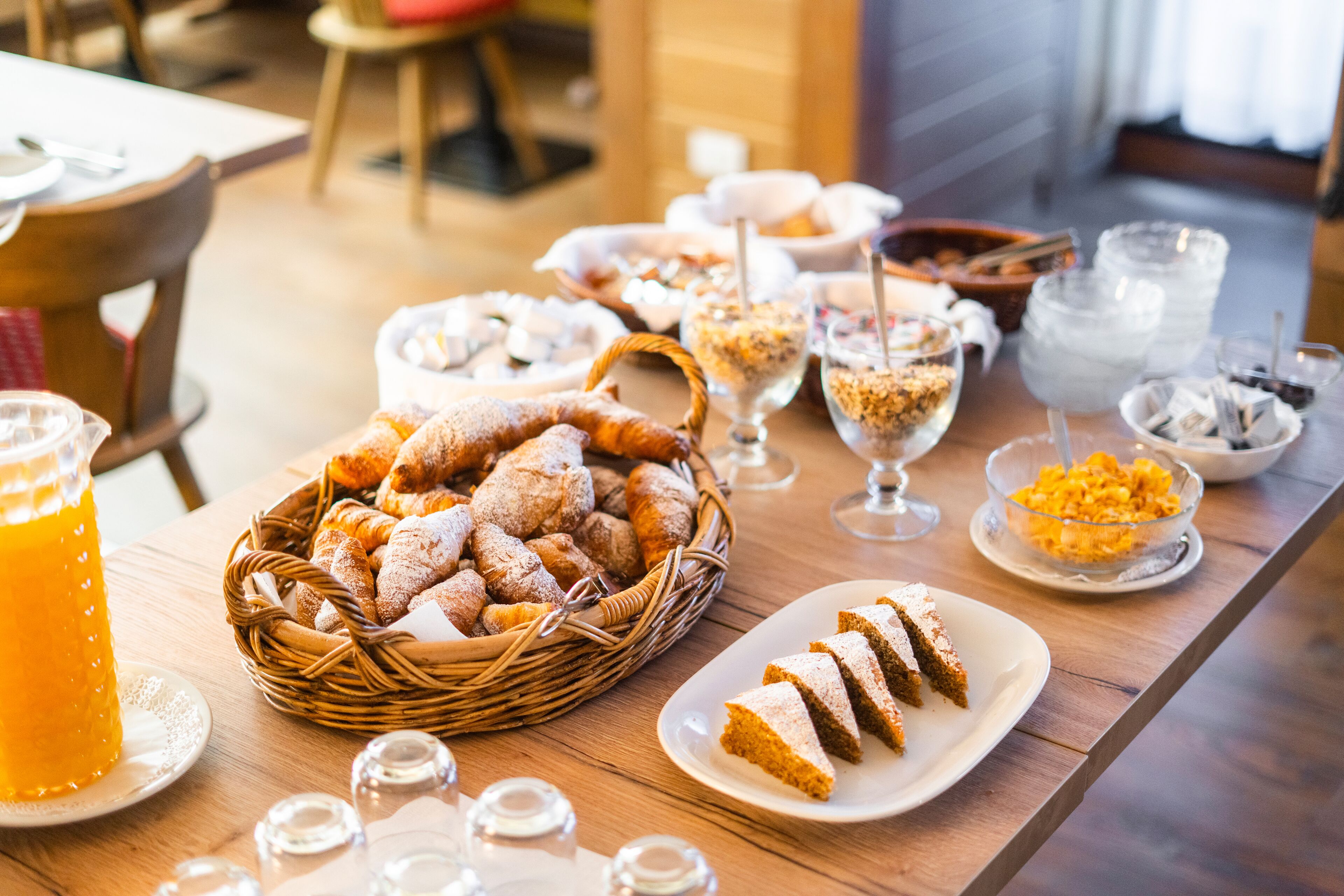 Un buffet de petit-déjeuner proposant une variété de viennoiseries, de pains et de boissons, le tout disposé sur une table en bois.