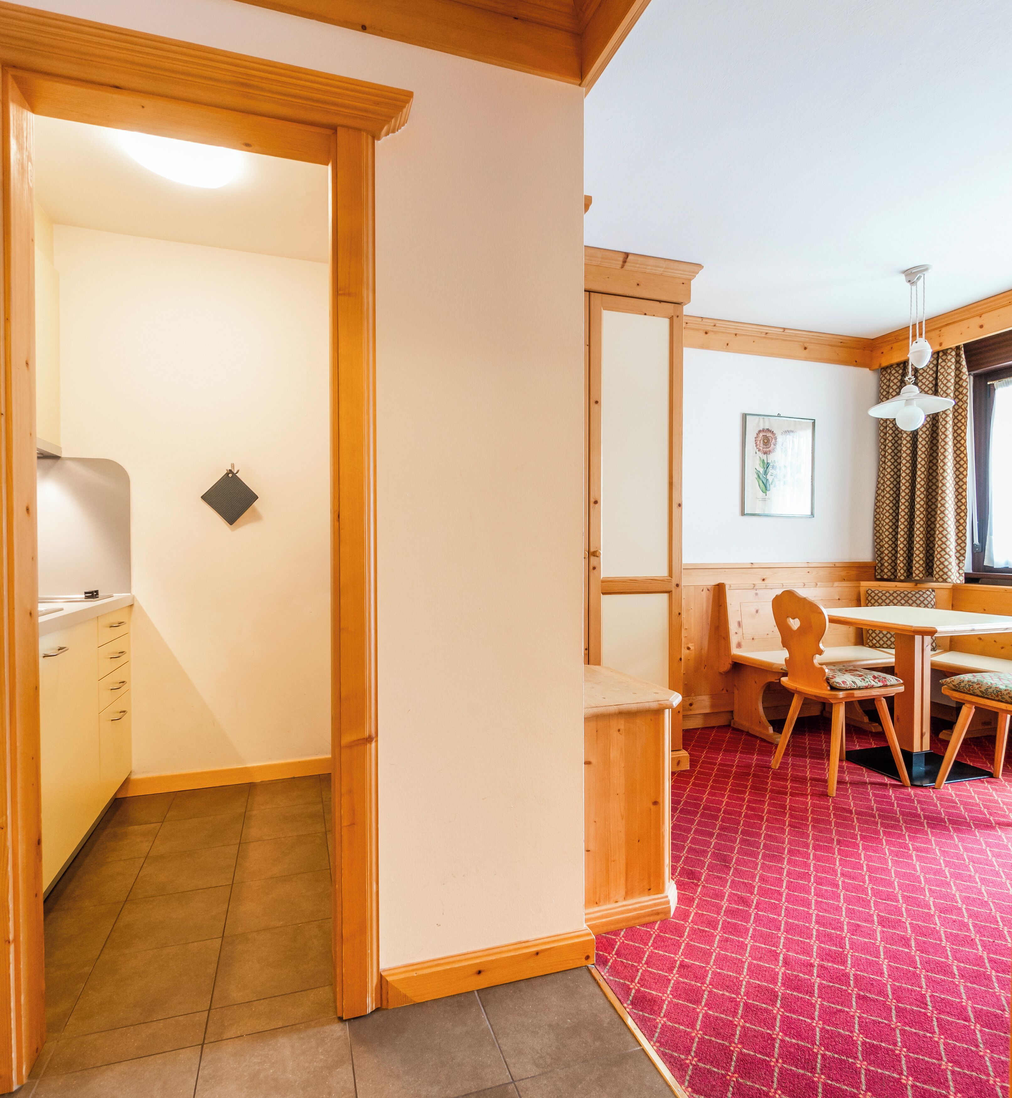 A room with a wooden bench, a table, and a red patterned carpet.