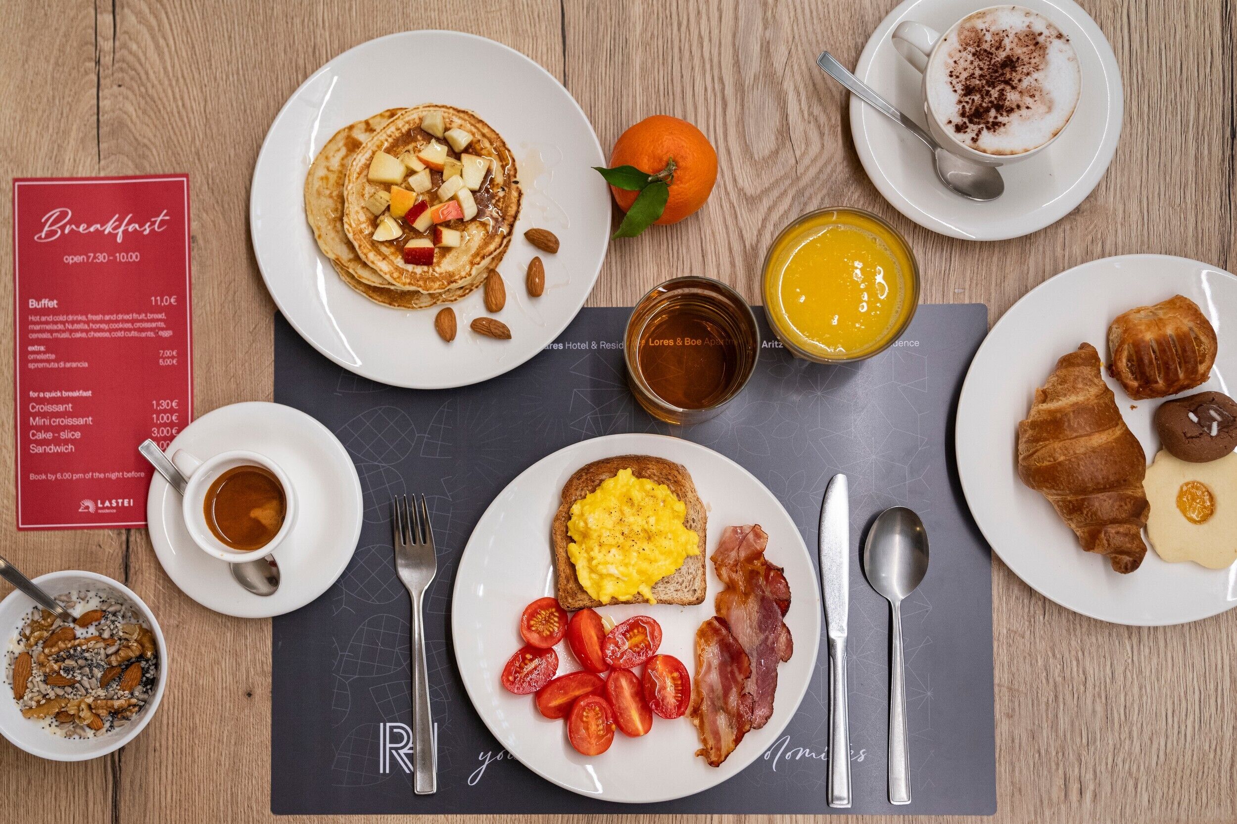 A breakfast setting with pancakes, toast, bacon, eggs, tomatoes, and orange juice on a wooden table.