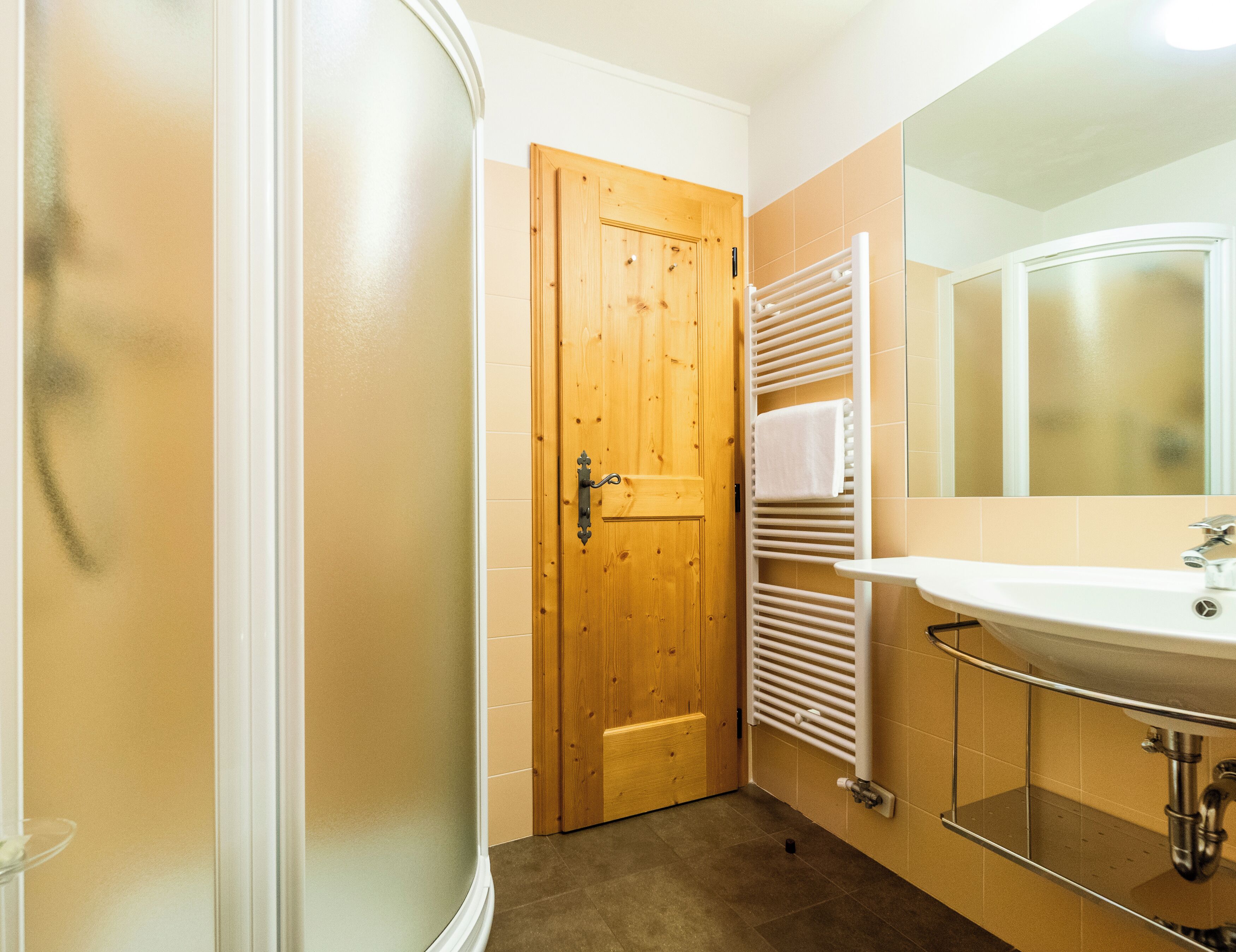 A bathroom with a wooden door, a white towel rack, a sink, and a mirror.
