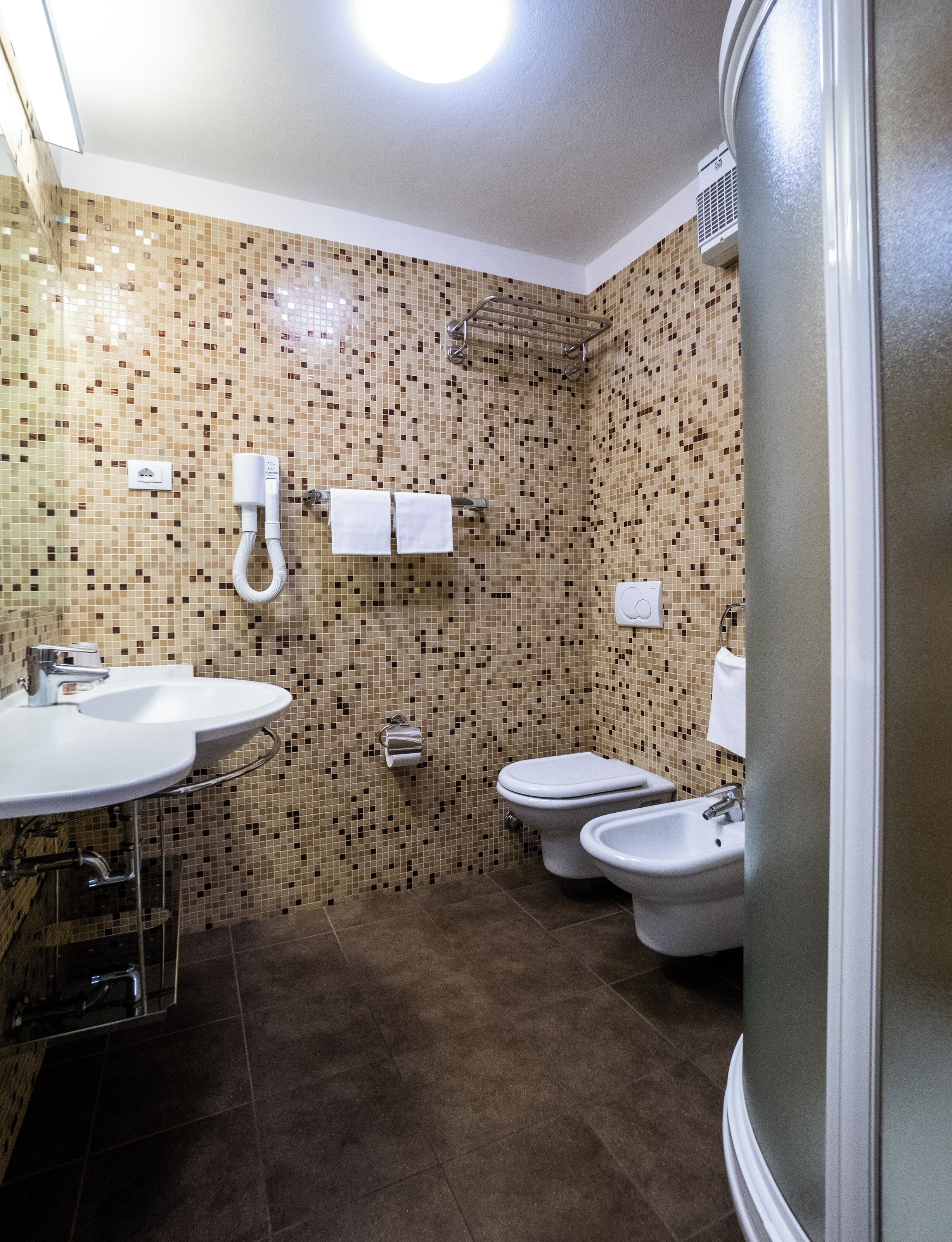 Une salle de bain avec un mur recouvert d’une mosaïque, un lavabo, des toilettes, un bidet et une douche.
