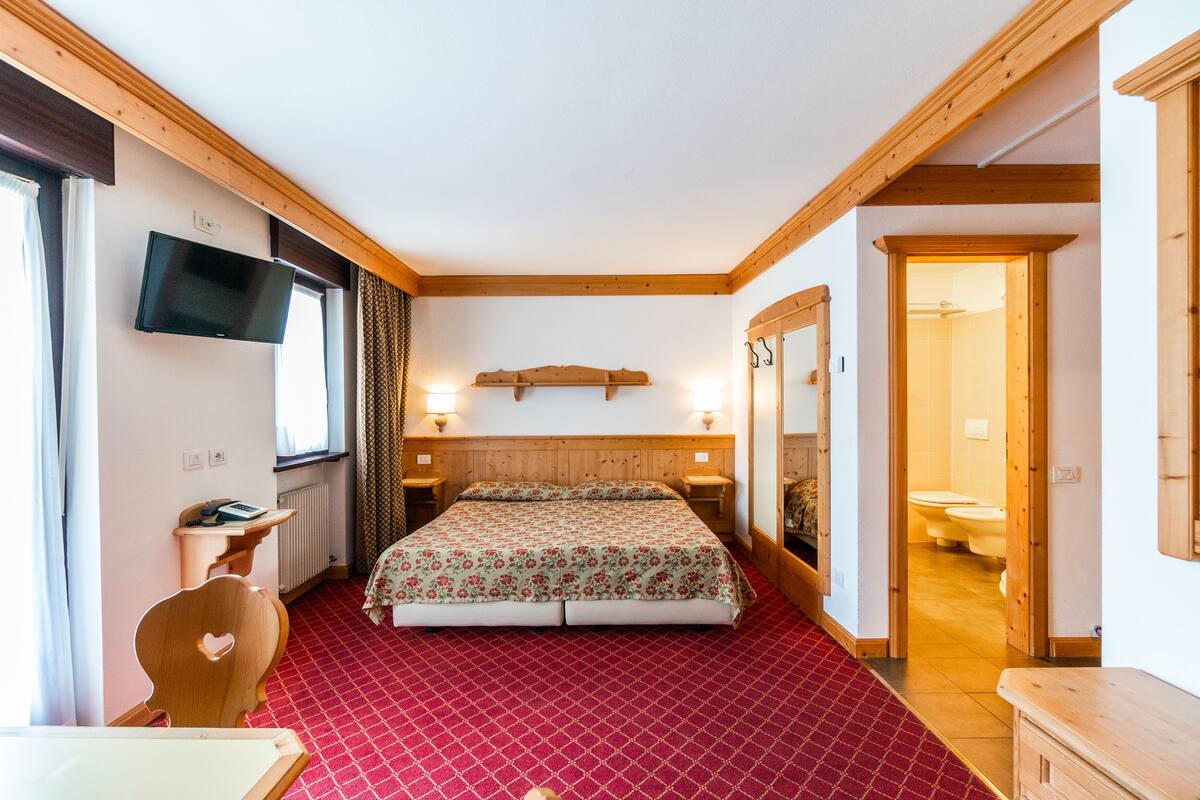 A hotel room with a bed, a TV mounted on the wall, a desk, and a chair.